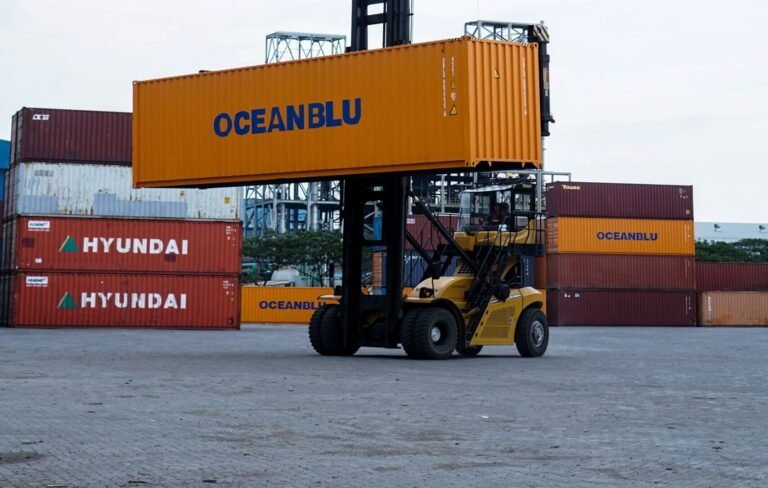 Forklift handling container in bustling Jakarta port with clear skies.